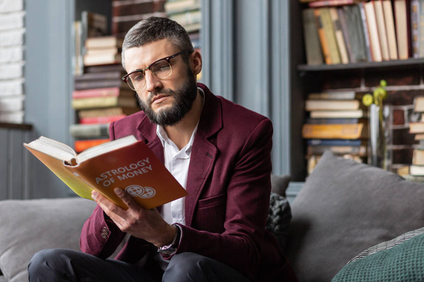 Man feeling thoughtful while reading book about astrology of money - Foto, immagini
