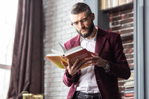 Stylish handsome man standing near window while reading book - Foto, immagini