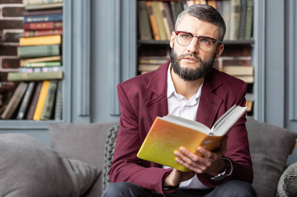 Dark-eyed bearded man feeling inspired after reading interesting book - Foto, afbeelding