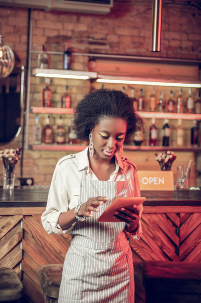 Pleasing alluring slim young African-American waitress checking information on tablet - Photo, image