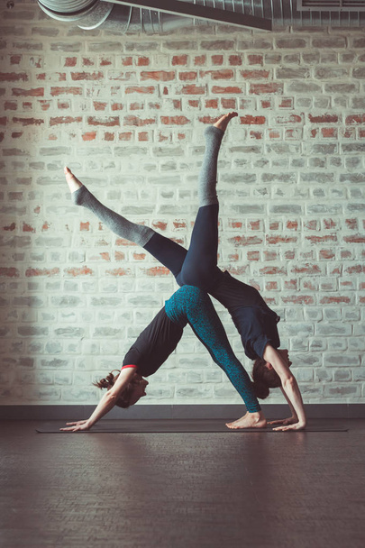 two beautiful caucasian women doing partner yoga in yoga studio opposite brick wall - Foto, Bild