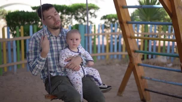 Zmęczony tata zamyka jego Eys siedzi na huśtawce z zmęczonym dzieckiem w zwolnionym tempie - Materiał filmowy, wideo