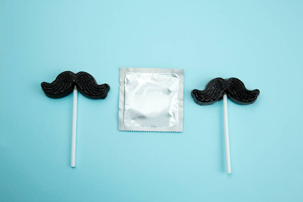 top view flat lay caramel on a stick in the shape of a mustache and a condom on a blue background - Foto, Imagen