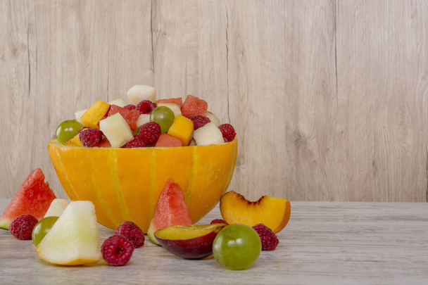 Fruit salad. Peach, watermelon, melon, raspberry, plum, grapes, diced lie in a melon salad bowl on a white wooden background. Pieces of fruit. Place for text. - Photo, Image