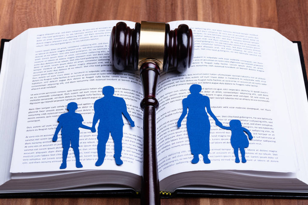 Blue Paper Cutout Of Separated Family On Open Book With Gavel Over Wooden Table - Foto, Bild