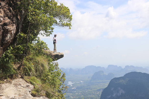 Ένας άνθρωπος στέκεται σε μια πέτρινη προεξοχή στα βουνά και με θέα τα βουνά κάτω, Krabi, Ταϊλάνδη. - Φωτογραφία, εικόνα
