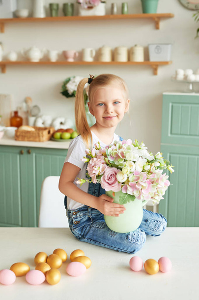 テーブルの上に座ってキッチンに花の花束を持つ少女 - 写真・画像