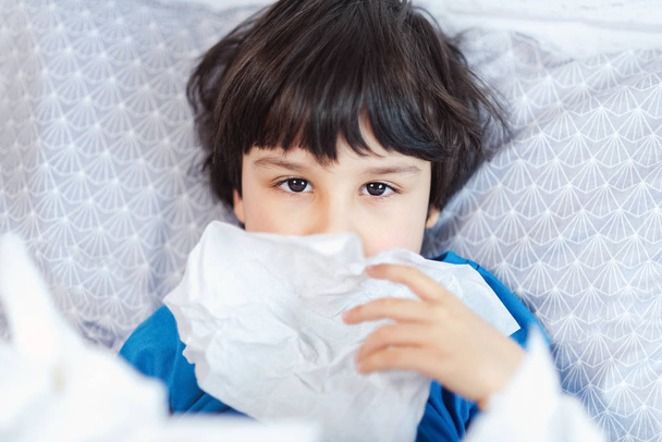 Niño enfermo con rinitis fría sonándose la nariz con servilleta en la cama, concepto de temporada de gripe
  - Foto, imagen