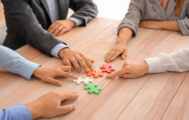Команда бизнесменов собирает головоломки на деревянном столе
 - Фото, изображение