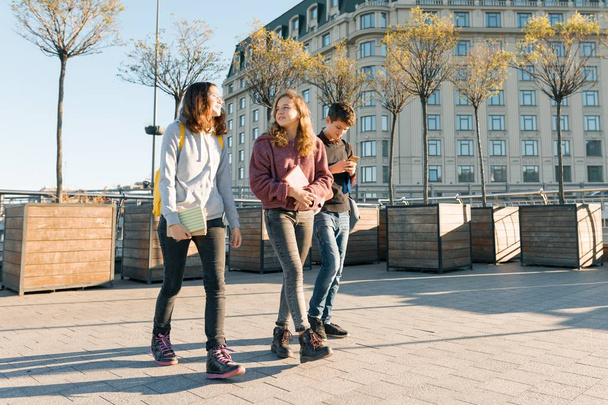 Outdoor portrait of teenage students with backpacks walking and talking. City background, golden hour - Photo, image
