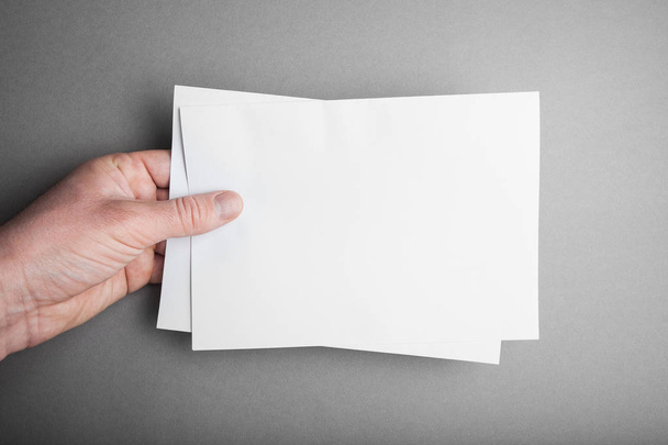 Empty blank paper mockup in hand on grey background. - Fotografie, Obrázek