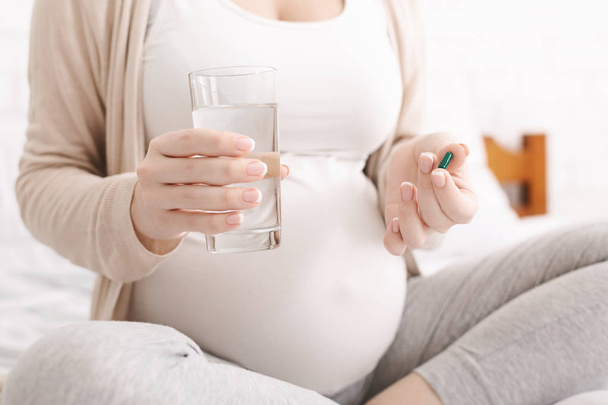 Pregnant woman holding pill and glass of water - Fotoğraf, Görsel