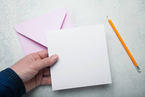 A square sheet of blank white paper in his hand, a pink envelope - Φωτογραφία, εικόνα