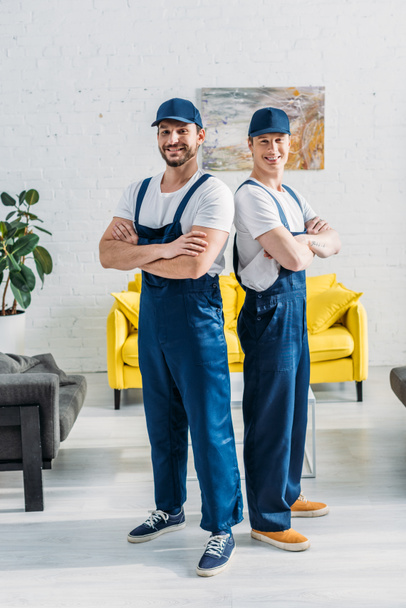 handsome movers with arms crossed looking at camera and smiling in apartment - Φωτογραφία, εικόνα