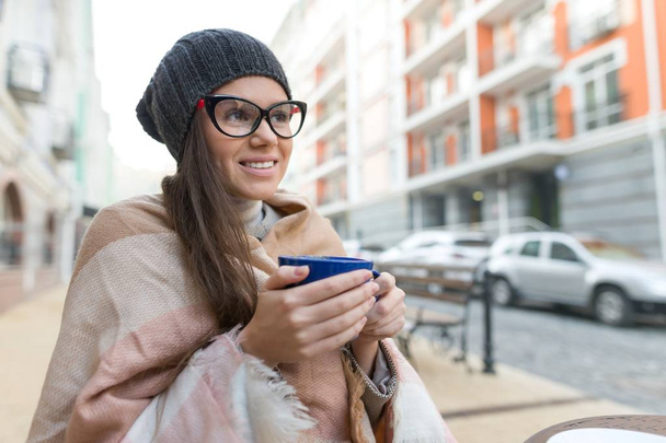 秋の冬の帽子の若い笑顔の女性、熱い飲み物をカップで肖像。シティストリートの背景 - 写真・画像