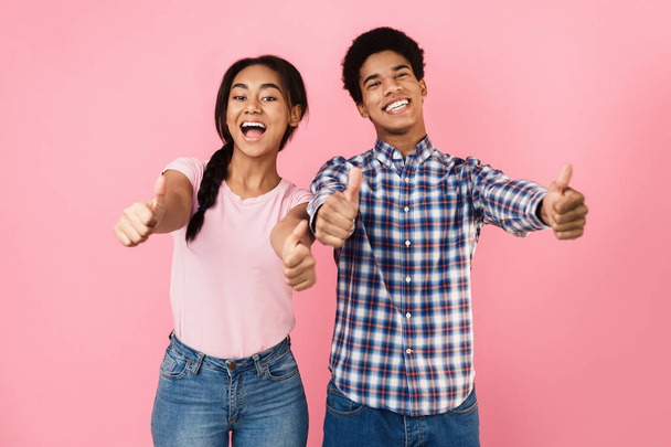 glückliches Teenager-Paar zeigt Daumen nach oben, rosa Hintergrund - Foto, Bild