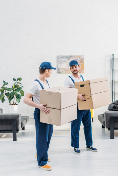 two movers in uniform carrying cardboard boxes in apartment with copy space - Photo, Image