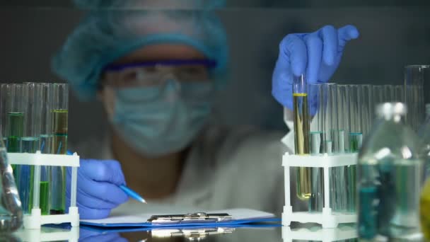 Laborassistentin überprüft Röhrchen mit gelber Flüssigkeit und schreibt Parfüm-Analysedaten - Filmmaterial, Video