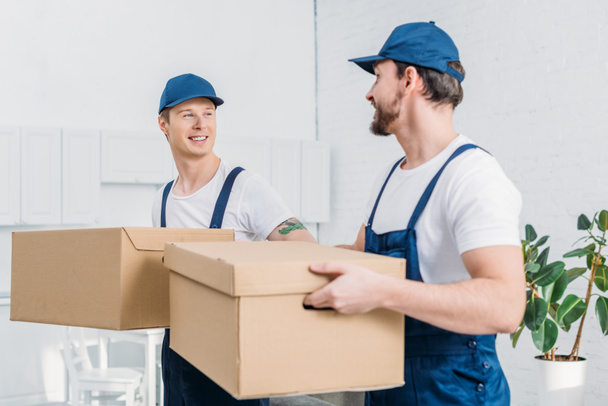 two smiling movers transporting cardboard boxes in apartment - Photo, Image