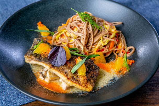 Buckwheat noodles on wok and baked carp. Asian cuisine. The work of a professional chef. Dish from a restaurant or cafe menu. Close-up - Foto, Bild