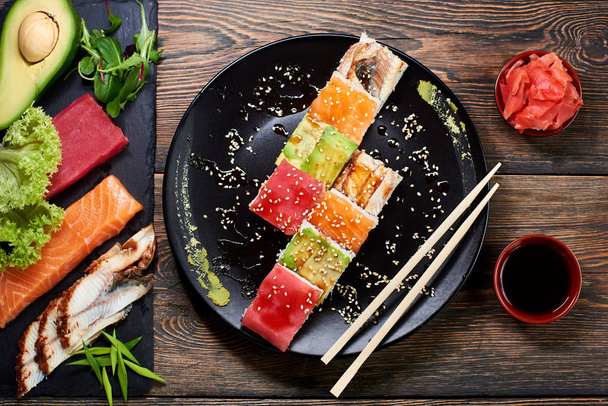 Крупный план вкусных суши с рисом и рыбой на черной тарелке подается на деревянном столе
 - Фото, изображение