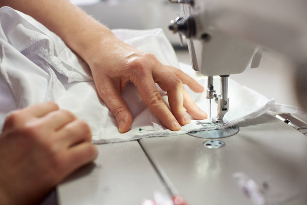 close up of female hands stitching white fabric on professional manufacturing machine at workplace - 写真・画像
