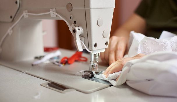 İşyerinde profesyonel üretim makinesinde beyaz kumaş dikiş eller, yakın çekim - Fotoğraf, Görsel