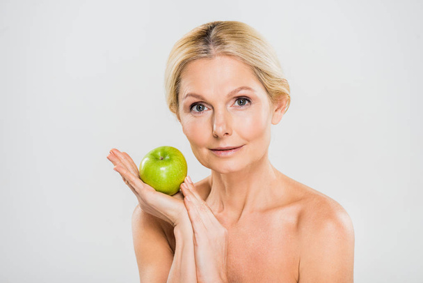 hermosa y madura mujer sosteniendo verde manzana madura y mirando a la cámara aislada en gris
 - Foto, Imagen