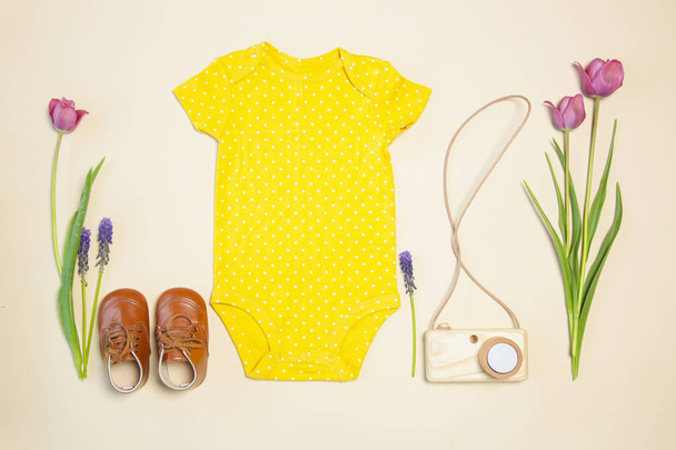 Baby spring outfit, vista dall'alto, corpo giallo, scarpe, macchina fotografica in legno giocattolo e tulipani rosa
 - Foto, immagini