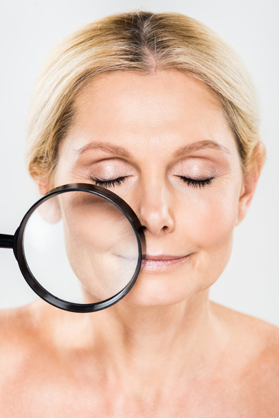 beautiful and blonde mature woman with closed eyes holding loupe isolated on grey - Photo, Image