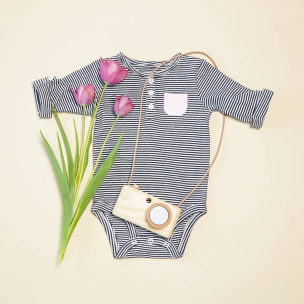 Baby Spring Outfit, Draufsicht, entblößter Körper, hölzernes Kameraspielzeug und rosa Tulpen - Foto, Bild