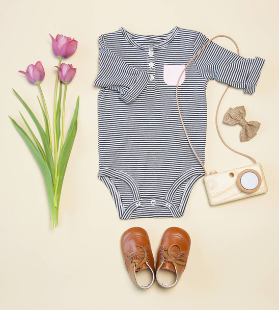 Traje de primavera de bebé, vista superior, cuerpo despojado, zapatos, juguete de cámara de madera y tulipanes rosados
 - Foto, Imagen
