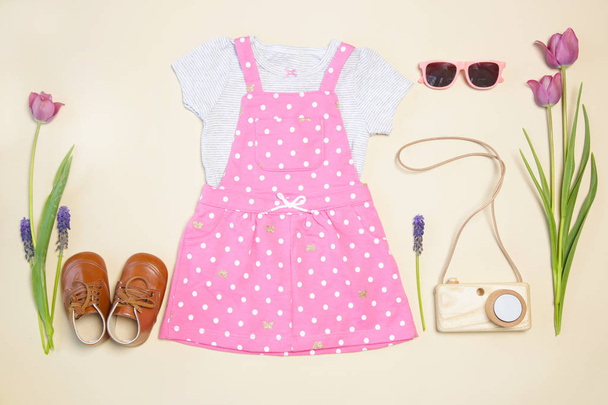 Traje de primavera de niña, vestido rosa, zapatos, juguete de cámara de madera y tulipanes rosados, vista superior
 - Foto, imagen