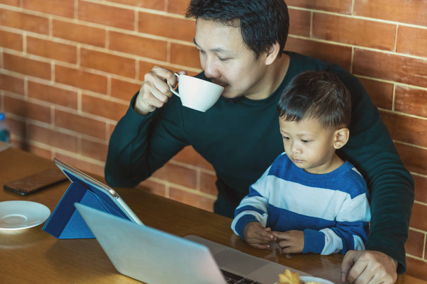 Asijský Jednolůžkový otec se synem se dívá na kreslený notebook přes technologii a pije kávu s prací, když žije v podkrovním domě pro Samučení nebo pro domácí školu, rodinu a Jednolůžkový koncept - Fotografie, Obrázek