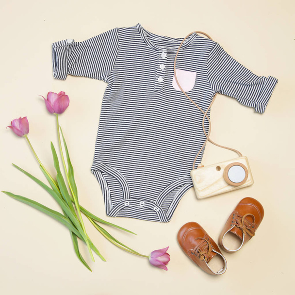 Babyfrühling-Outfit, Draufsicht, entblößter Körper, Schuhe, hölzernes Kameraspielzeug und rosa Tulpen - Foto, Bild