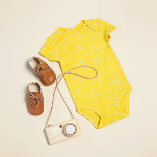 Roupa de mola de bebê, vista superior, corpo amarelo, sapatos e brinquedo de câmera de madeira
 - Foto, Imagem