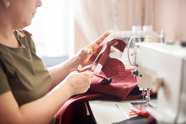 Main féminine utilisant des ciseaux pour couper la pièce textile dans le processus de couture
 - Photo, image