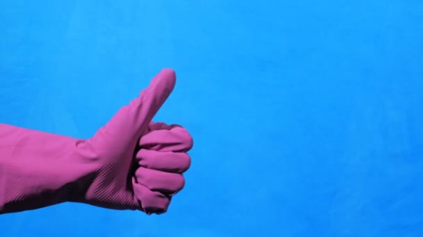 Cleaner hand in purple rubber glove on blue background. Like and dislike gesture. - Felvétel, videó