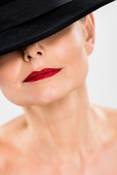 Selektivní fokus středního věku elegantní a módní ženy s červenými rty v černém klobouku, izolované Grey  - Fotografie, Obrázek