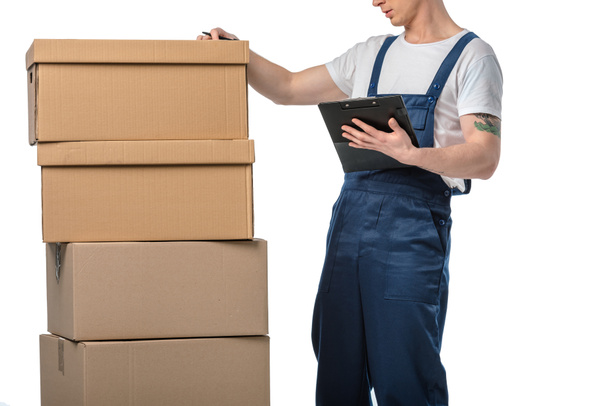 cropped view of mover in uniform holding clipboard near cardboard boxes isolated on white - Foto, Imagem