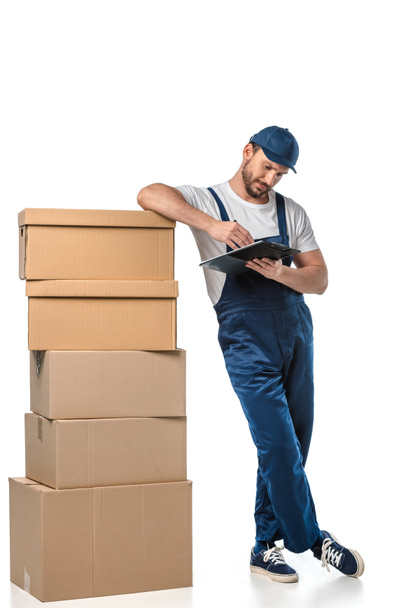 mover in uniform writing in clipboard near cardboard boxes isolated on white - Photo, Image
