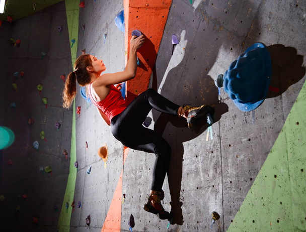Young Active Woman Bouldering on Colorful Artificial Rock in Climbing Gym. Extreme Sport and Indoor Climbing Concept - 写真・画像