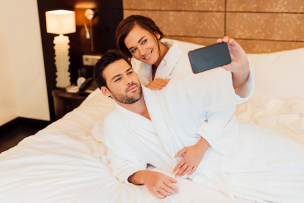 ベッドの上に横たわっている間フォンで幸せなカップル撮影 selfie  - 写真・画像