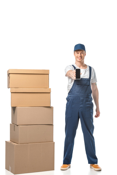 smiling mover with cardboard boxes showing smartphone with blank screen isolated on white - Photo, Image