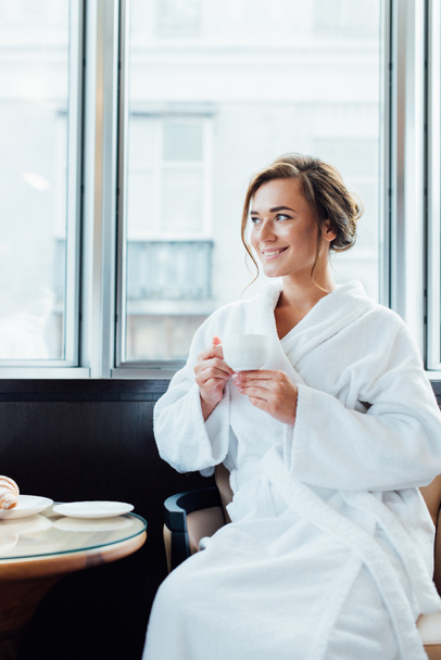 attractive brunette woman in bathrobe sitting and holding cup of coffee - 写真・画像
