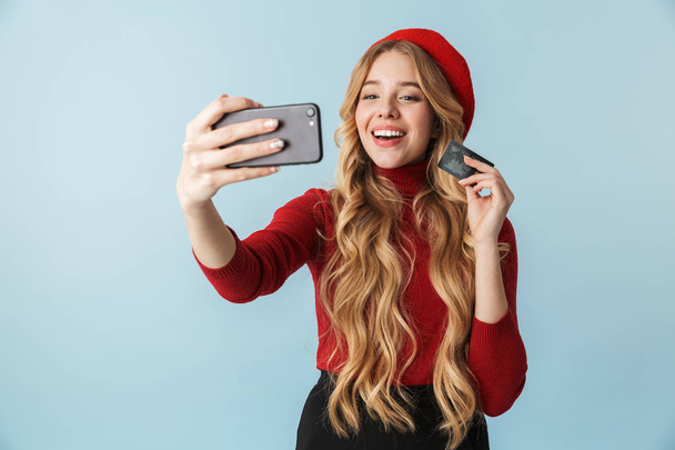 Modest blond woman 20s holding credit card while taking selfie p - Foto, afbeelding