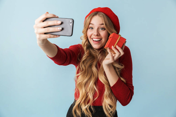Smiling blond woman 20s holding birthday box while taking selfie - Fotó, kép