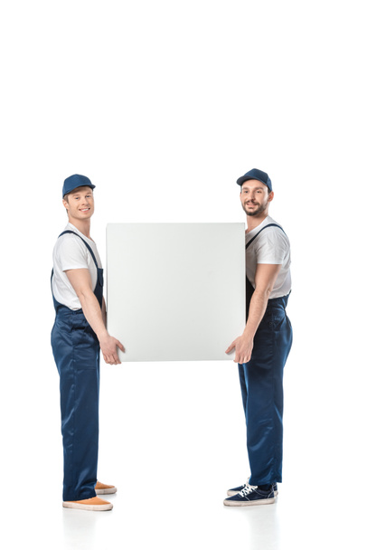 two smiling movers looking at camera while holding blank box isolated on white - Photo, Image