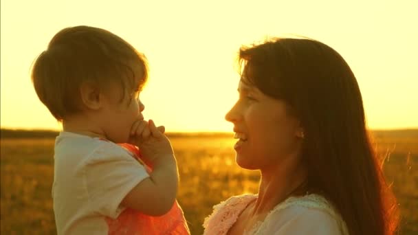 Mama spricht mit einer kleinen Tochter. das Kind sitzt in den Armen der Mutter. glückliche Familienspaziergänge im Frühling, Sommer bei Sonnenuntergang, die goldene Sonne. Zeitlupe. Glückliches Familienkonzept - Filmmaterial, Video
