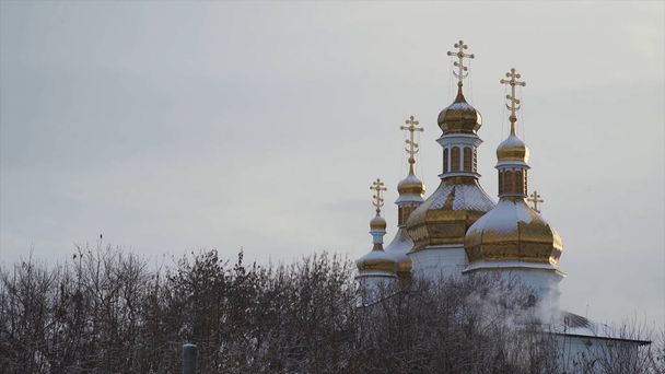 Iglesia grande y hermosa con nieve sobre cúpulas doradas sobre fondo claro y gris del cielo. Acciones. Paisaje invernal de la Catedral de pie entre los árboles
. - Foto, imagen